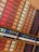 A neatly organized display of various coffee pods arranged in rows and columns on a wooden surface. The pods are housed in colorful packaging, varying from red, orange, and cream to darker shades. Below the pods, there are rows of capsules and promotional materials likely detailing different coffee flavors.