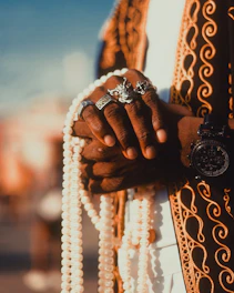 A close-up of mah’s hands delicately threading semi-precious stones onto a vintage-inspired bracelet, surrounded by pressed flowers and aged parchment.