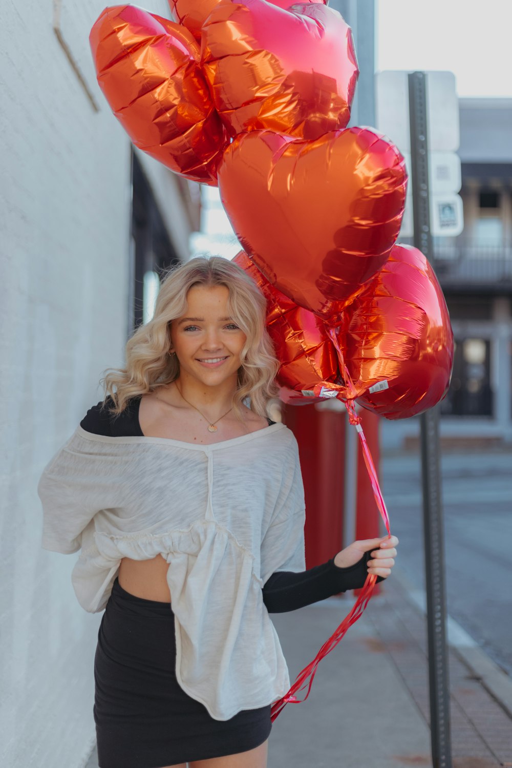 a woman holding a bunch of red heart shaped balloons