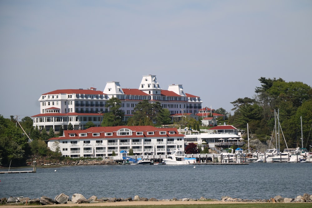 a large white building with a red roof next to a body of water