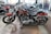 Several sleek, red motorcycles are parked in a showroom with polished concrete floors. The motorcycles have chrome accents and black seats, and are lined up in an orderly fashion. The showroom has large windows and other motorcycles visible in the background.