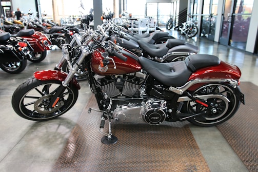 Several sleek, red motorcycles are parked in a showroom with polished concrete floors. The motorcycles have chrome accents and black seats, and are lined up in an orderly fashion. The showroom has large windows and other motorcycles visible in the background.