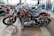 Several sleek, red motorcycles are parked in a showroom with polished concrete floors. The motorcycles have chrome accents and black seats, and are lined up in an orderly fashion. The showroom has large windows and other motorcycles visible in the background.