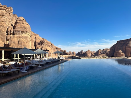 Guests lounging by a sleek infinity pool with deep blue water blending into the ocean backdrop.
