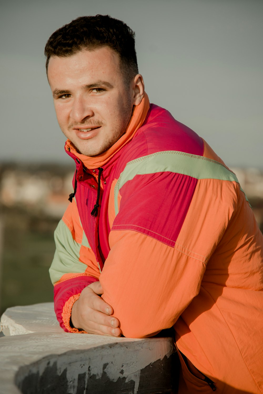 a man in an orange and pink jacket leaning on a wall