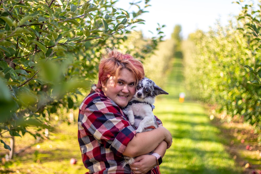 a woman holding a small dog in an apple orchard