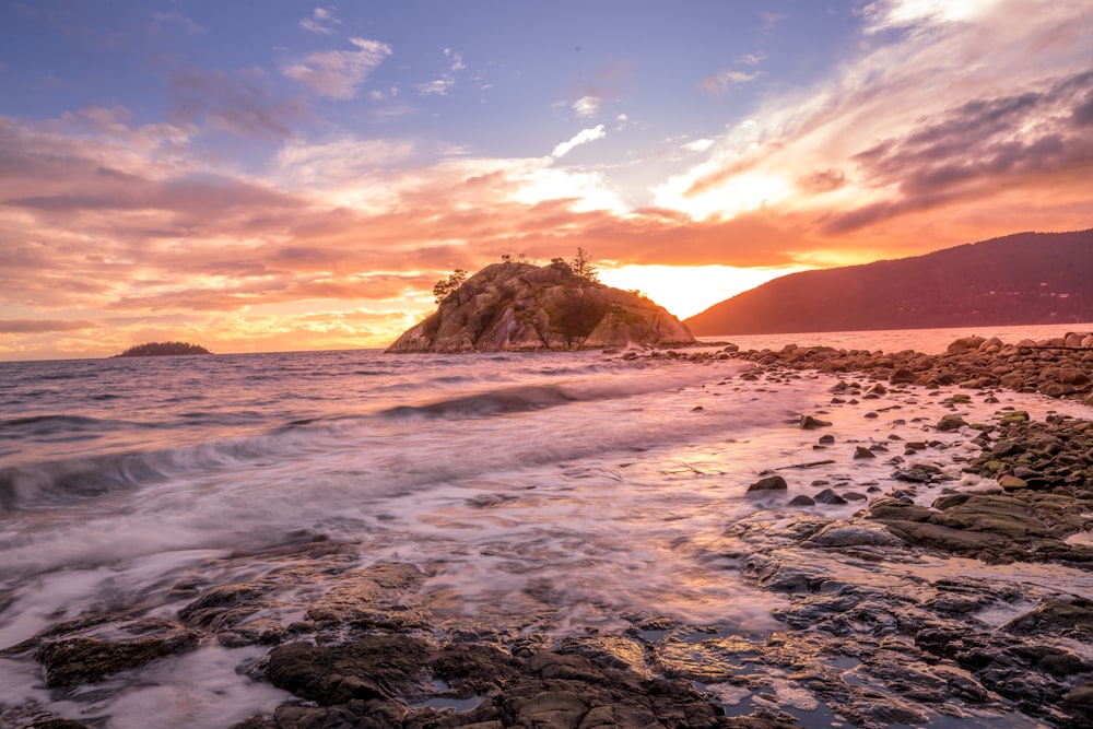 the sun is setting over a rocky beach