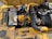 A detailed view of a yellow industrial engine with various components, including hoses, a fan belt, and metallic parts. There is a prominent use of black and yellow materials, and the engine is set against a sunny background which casts shadows on its surface.