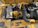A detailed view of a yellow industrial engine with various components, including hoses, a fan belt, and metallic parts. There is a prominent use of black and yellow materials, and the engine is set against a sunny background which casts shadows on its surface.