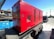 A large red generator is mounted on a trailer, parked in an industrial area with a blue dumpster nearby. In the background, a black pickup truck and a utility pole are visible under a clear blue sky. The ground is paved with concrete.