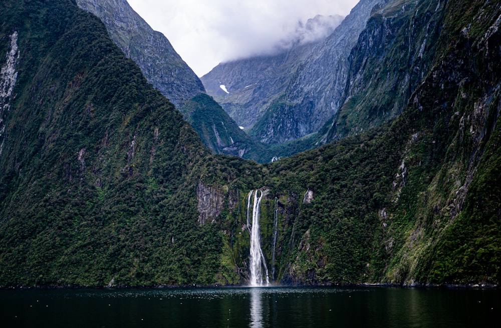a waterfall in the middle of a river surrounded by mountains