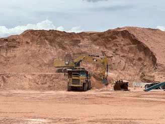 Heavy-duty truck loading sand at a construction site under a clear sky.