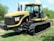 A Caterpillar agricultural tractor with large rubber tracks is parked on grass. The machine has a sleek yellow and black design, with the recognizable CAT logo on the side. The tractor features a spacious cabin with large windows and various machinery parts are visible.