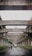 A view under a series of concrete overpasses, showing a road with vehicles including a van and motorcycles. The road is wet, suggesting recent rain. Signs on the left indicate directions to Surabaya and Pondok Taman, amidst greenery lining the road.