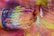 Close-up of a paintbrush with bristles coated in vibrant, multicolored paint resting on a surface covered in the same hues. The colors blend together, creating a dynamic spectrum with textures that suggest movement and creativity.