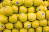 A large pile of yellow apples, each with a small blue sticker attached, is stacked together. The apples appear fresh and shiny, making them visually appealing.