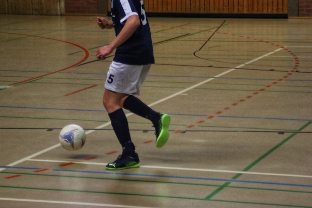 a young man kicking a soccer ball on a gym floor