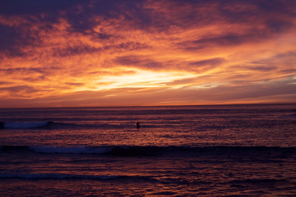 a sunset over the ocean with a surfer in the distance