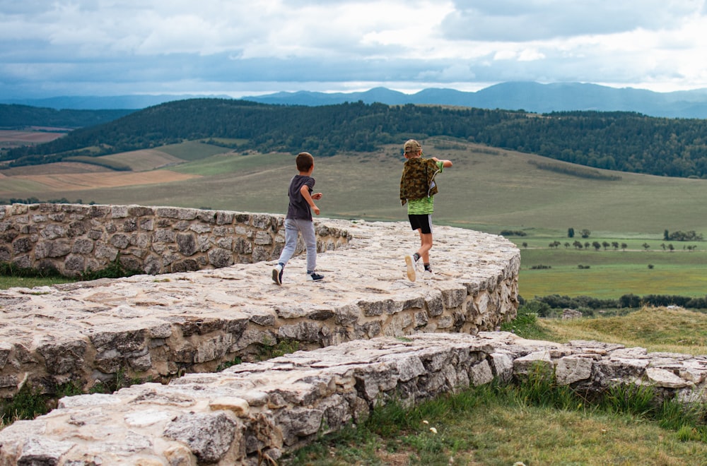 a couple of kids standing on top of a stone wall