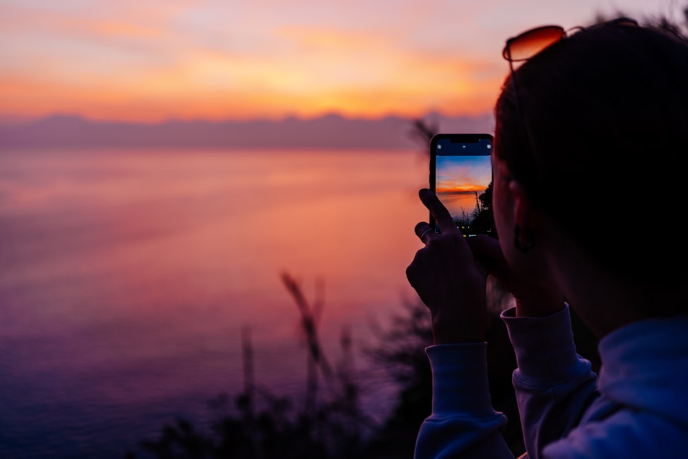 a woman taking a picture of a sunset with her cell phone