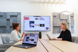 two women sitting at a table with a laptop