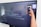 A person is holding a smartphone to take a picture of a large screen displaying a social media post. The content on the screen talks about increasing real-time engagement at a large event called GearFest. In the top corner, there's a QR code and a prompt to create a post.
