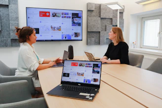 two women sitting at a table with a laptop