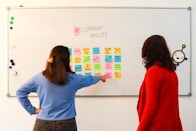 a couple of women standing in front of a white board