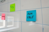 A whiteboard features a grid layout with blue lines and has colorful sticky notes attached to it. The sticky notes include a blue one labeled 'FUN FACT,' a green one labeled 'Funny,' and a pink one labeled 'CULTURE.'