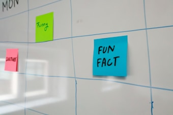 A whiteboard features a grid layout with blue lines and has colorful sticky notes attached to it. The sticky notes include a blue one labeled 'FUN FACT,' a green one labeled 'Funny,' and a pink one labeled 'CULTURE.'