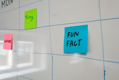A whiteboard features a grid layout with blue lines and has colorful sticky notes attached to it. The sticky notes include a blue one labeled 'FUN FACT,' a green one labeled 'Funny,' and a pink one labeled 'CULTURE.'