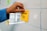 A hand places a yellow sticky note with the words 'How-To' written on it onto a whiteboard. The whiteboard features a grid pattern, and there are other colorful sticky notes attached.