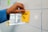 A hand places a yellow sticky note with the words 'How-To' written on it onto a whiteboard. The whiteboard features a grid pattern, and there are other colorful sticky notes attached.