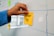 A hand places a yellow sticky note with the words 'How-To' written on it onto a whiteboard. The whiteboard features a grid pattern, and there are other colorful sticky notes attached.