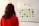 A person with long hair wearing a red sweater is observing a whiteboard. On the whiteboard, there is an arrangement of multi-colored sticky notes with various words and phrases related to company values, such as 'equity', 'teamwork', 'respect', and 'diversity'. The words '# COMPANY VALUES' are prominently written at the top.