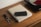 A wooden table holds a beige book titled 'The Monocle Guide to Good Business,' accompanied by a black wallet on top. Next to the book is a keychain with keys and a leather strap. In the background, part of a turntable is visible with a vinyl record on it.