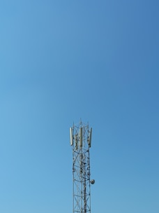 A tall communication tower stands against a clear blue sky. The structure is composed of a metal framework with several antennas and dishes attached to it.