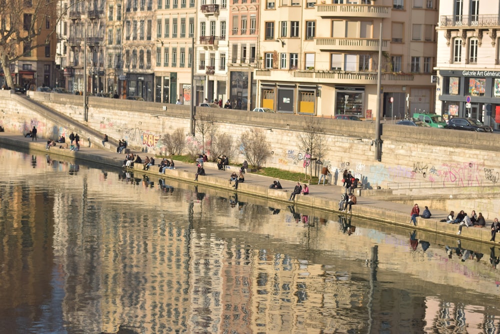 a group of people walking along a river next to tall buildings