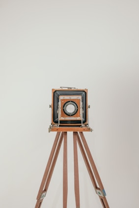 A vintage tintype camera set up on a wooden tripod with soft natural light highlighting its intricate details.