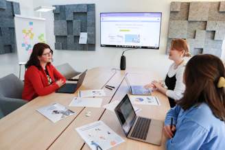 a group of people sitting around a table with laptops