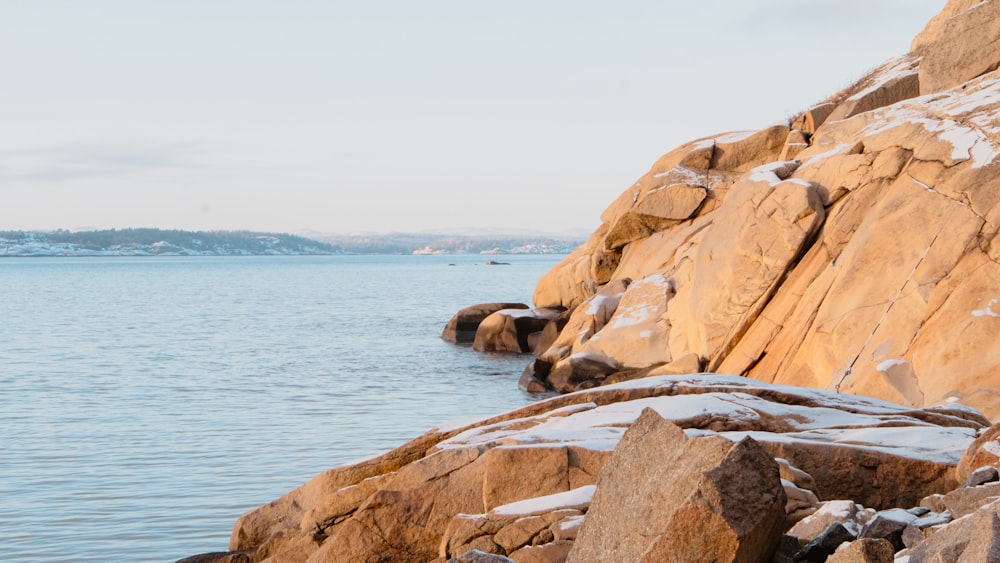 a rocky shoreline covered in snow next to a body of water