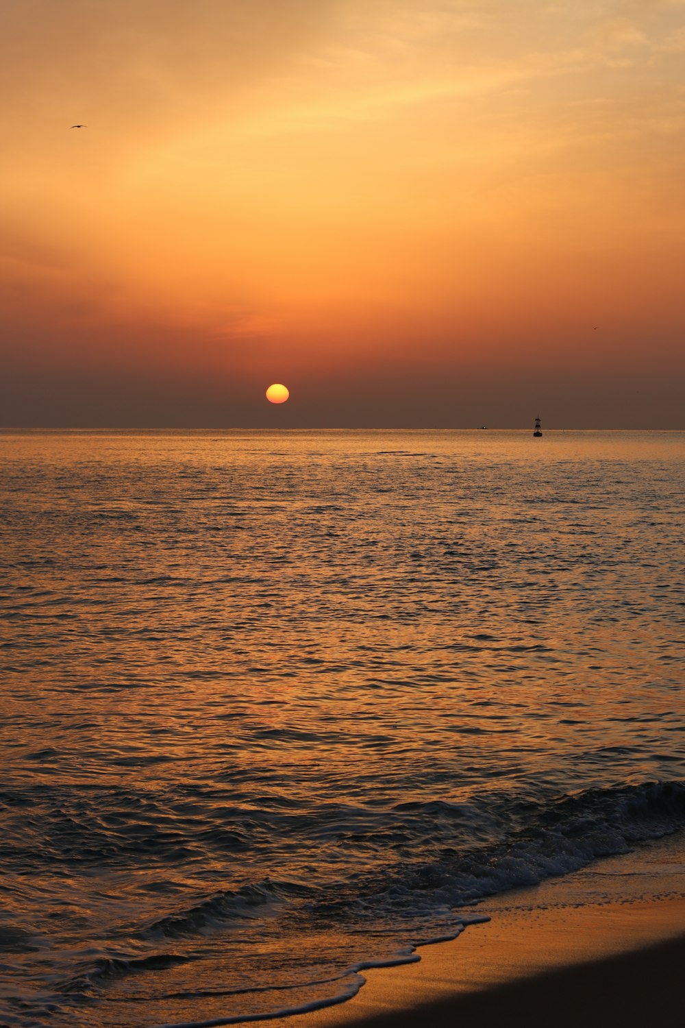 the sun is setting over the ocean with a boat in the distance