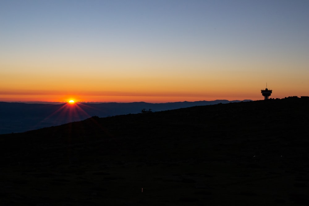 the sun is setting over a hill with a tower in the distance