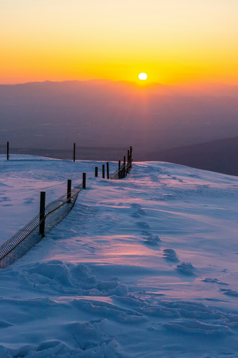 the sun is setting over a snowy hill