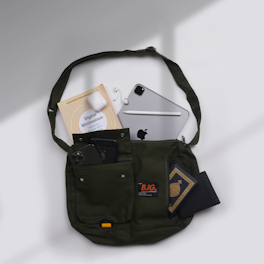 A green shoulder bag containing various items, including a book titled 'Digital Minimalism,' an iPad with an Apple Pencil, AirPods, a smartphone, a black wallet, and another book with decorative elements on the cover. The bag is neatly arranged and displayed on a white surface with soft shadows.