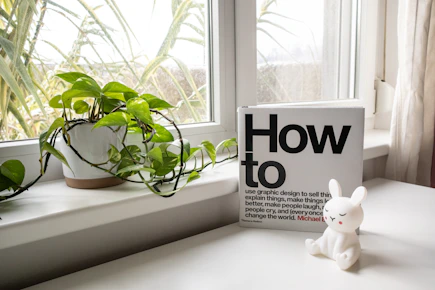 a white rabbit figurine sitting on a window sill next to a book