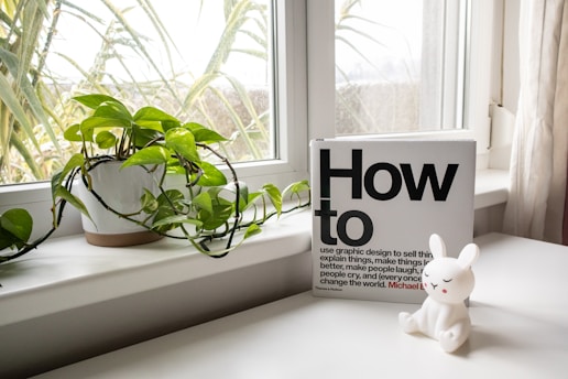 a white rabbit figurine sitting on a window sill next to a book