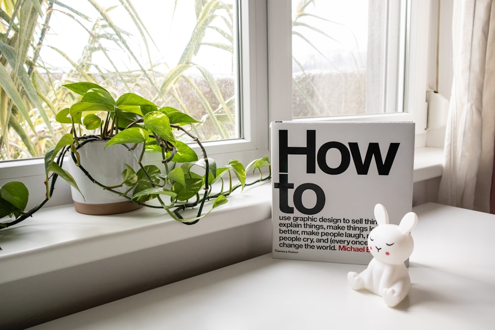 a white rabbit figurine sitting on a window sill next to a book