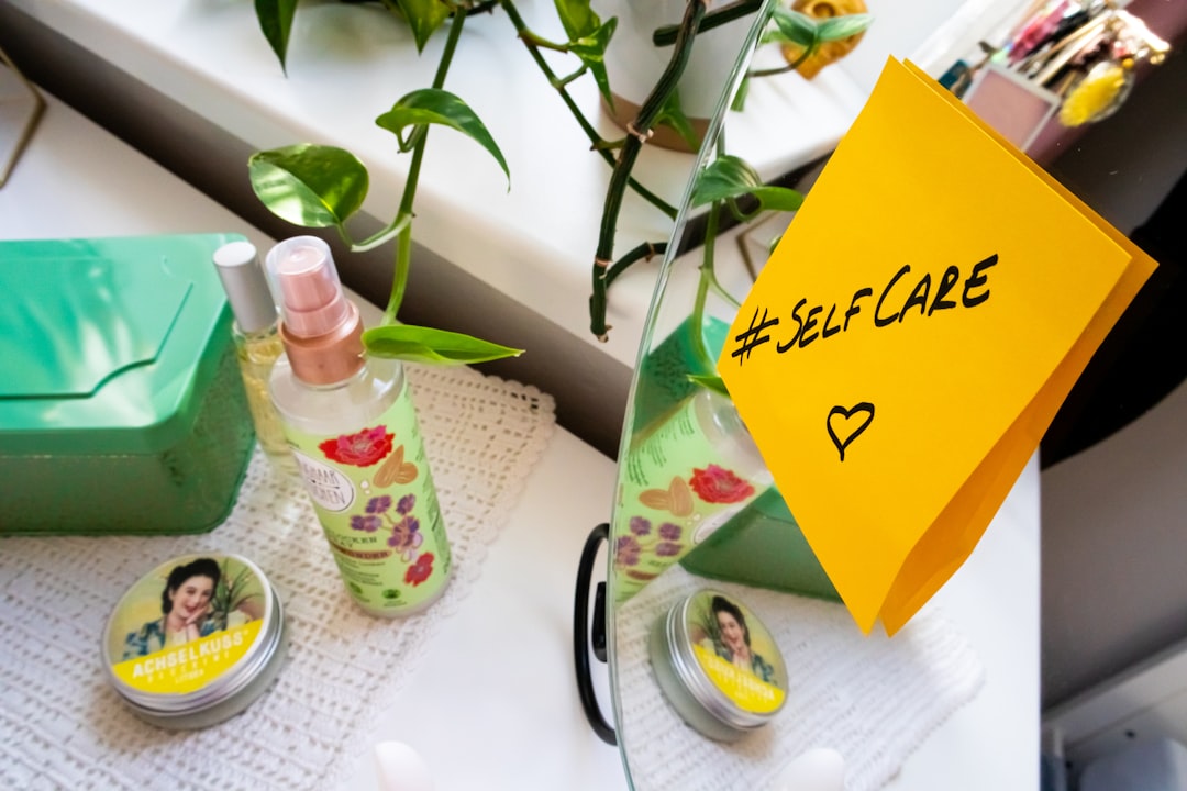 a close up of a bottle of lotion on a table, Dresser with cosmetic products and a mirror with a sticky note with the hashtag #selfcare on it