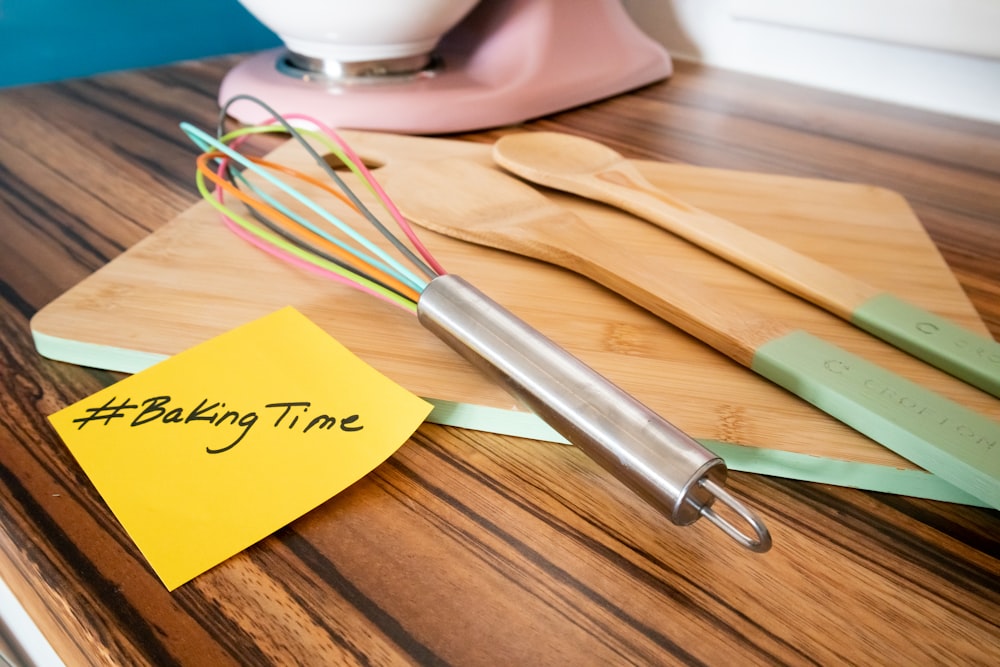 a wooden table topped with a whisk and a yellow post it note